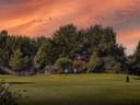 Zwei Personen auf einem Golfplatz bei Sonnenuntergang mit Bäumen im Hintergrund.