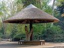 Grosser, pilzförmiger Pavillon mit Strohdach im Park.