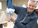 Mann hält Netz voller Golfbälle und lächelt.