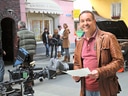 Mann auf einem Filmset mit Kamera und Crew im Hintergrund.