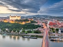 Blick auf beleuchtete Burg und Stadt am Fluss bei Abenddämmerung.
