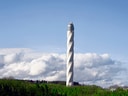 Schraubenförmiger Turm über grüner Landschaft, bewölkter Himmel.