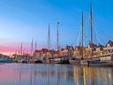 Hafen mit Segelschiffen bei Sonnenuntergang, traditionelle Gebäude im Hintergrund.