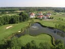 Luftaufnahme eines Golfplatzes mit Teich und Gebäuden im Hintergrund.
