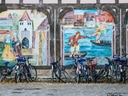 Fahrräder vor einer bemalten Wand mit historischen Szenen.