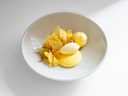 Weisser Teller mit kunstvoll angerichteten gelben Desserts.
