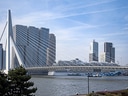 Moderne Brücke und Kreuzfahrtschiff vor Stadtsilhouette am Fluss.