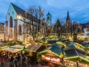 Weihnachtsmarkt mit beleuchteten Buden und Kirche im Hintergrund.