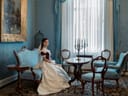Frau in historischer Kleidung sitzt in einem elegant eingerichteten Raum mit blauen Möbeln.