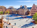Historischer Platz mit alten Gebäuden und Menschen in sonnigem Wetter.