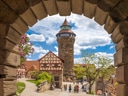 Blick durch Torbogen auf mittelalterlichen Turm und Fachwerkhaus mit Menschen.