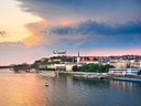 Flusslandschaft mit Burg und Stadtansicht bei Sonnenuntergang.