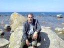 Mann in Anzug sitzt auf Felsen am Meer.