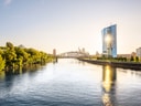 Flusslandschaft mit Brücke und modernen Gebäuden bei Sonnenuntergang.