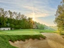 Sonnenaufgang über einem Golfplatz mit Bunker und Bäumen.