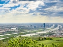 Stadtansicht mit Fluss und grünem Vordergrund bei bewölktem Himmel.