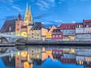 Stadtansicht mit historischen Gebäuden und Turm, reflektiert im Wasser.