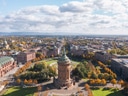 Luftaufnahme eines historischen Turms in einem Stadtzentrum mit umliegenden Parks und Gebäuden.
