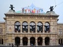 Historisches Gebäude mit Bögen und Statuen, davor Menschen und ein Radfahrer.