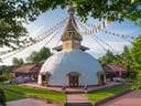 Weisser Stupa mit Gebetsfahnen im Garten.