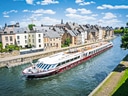 Boot fährt auf Fluss neben alten Gebäuden.