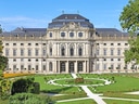 Barockpalast mit gepflegtem Garten und blauem Himmel.