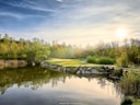 Sonnenuntergang über einem Teich mit Brücke und Bäumen.