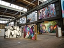 Industriehalle mit ausgestellten Gemälden und Wandkunst an den Wänden.