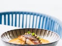 Schüssel mit einem Fischgericht auf einem Tisch, im Hintergrund ein blauer Stuhl.