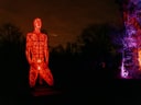 Leuchtende rote Statue in der Nacht, umgeben von bunt beleuchteten Bäumen.