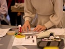 Person arbeitet an einem Tisch voller Papiere und Werkzeug.