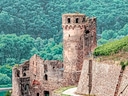 Mittelalterliche Burgruine mit Turm vor bewaldetem Hintergrund.
