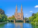 Kirche mit zwei Türmen, Fluss und Brücke im Vordergrund.