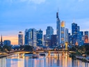 Skyline von Frankfurt am Main am Abend mit beleuchteten Hochhäusern und Fluss.