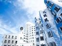 Moderne Gebäudefassade neben einem Fernsehturm unter blauem Himmel.
