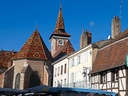 Blick auf Gebäude mit bunten Dächern und einem Kirchturm bei blauem Himmel.