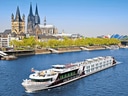 Flussschiff auf einem Fluss vor einer Stadt mit historischen Gebäuden und einer grossen Kirche.