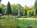 Menschen spazieren in einem gepflegten Garten mit Springbrunnen und Bäumen.