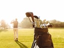 Golftasche auf Rasen, Person im Hintergrund golfend.