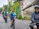 Gruppe von Menschen beim Radfahren in einem Dorf mit Steinhäusern.