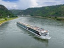Kreuzfahrtschiff auf einem Fluss zwischen grünen Hügeln.