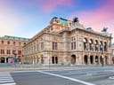 Historisches Gebäude mit verzierten Fassaden vor blauem und rosa Himmel.