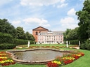 Barockgebäude mit Garten und Teich, umgeben von Bäumen.