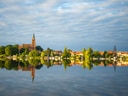 Stadtlandschaft am See mit Kirche und Wolkenhimmel.