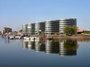 Moderne runde Gebäude am Flussufer mit Spiegelung im Wasser.