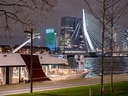 Beleuchtetes Kreuzfahrtschiff vor Erasmusbrücke in Rotterdam bei Nacht.