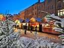 Verschneiter Weihnachtsmarkt mit geschmückten Buden und Menschen.
