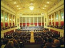 Innenansicht eines grossen Konzertsaals mit Publikum und Orchester auf der Bühne.