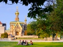 Menschen sitzen auf Rasen vor russisch-orthodoxer Kapelle in sonnigem Park.