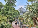 Zwei Personen gehen in einem botanischen Garten mit Gewächshaus.